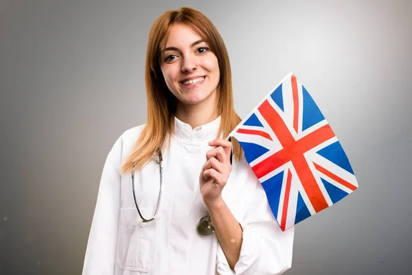 若い医者灰色の背景に英国のフラグを保持している女性 — ストック写真