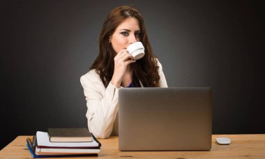 Onu laptop ile çalışan ve bir fincan kahve siyah arka plan üzerinde tutan bir iş kadını