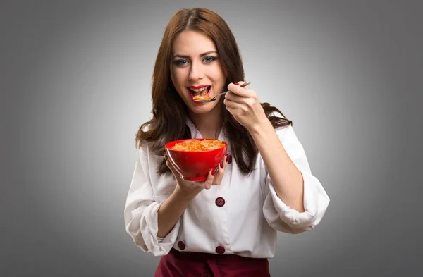 Mulher chef bonita comendo cereais de uma tigela em fundo cinza — Fotografia de Stock