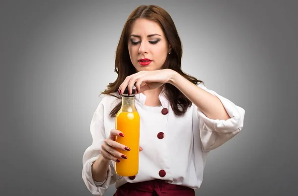 Bir portakal suyu gri arka plan üzerinde tutan güzel şef kadın — Stok fotoğraf