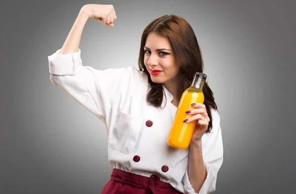 美丽的厨师妇女拿着橙汁在灰色背景 — 图库照片