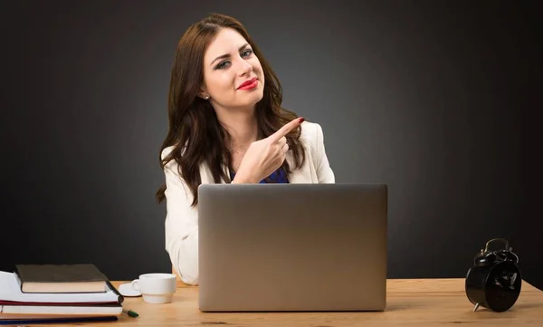 Mujer de negocios trabajando con su portátil y apuntando hacia el lateral sobre fondo negro —  Fotos de Stock