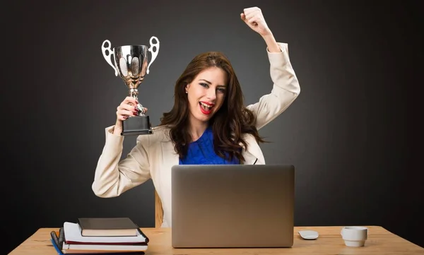 Деловая женщина работает со своим ноутбуком и держит трофей на черном фоне — стоковое фото