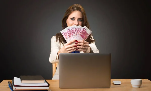 Mujer de negocios trabajando con su portátil y tomando un montón de dinero en el fondo negro — Foto de Stock