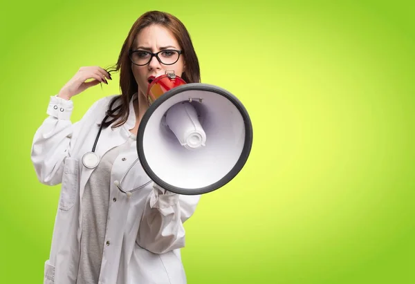 Dokter vrouw schreeuwen door megafoon op groene achtergrond — Stockfoto