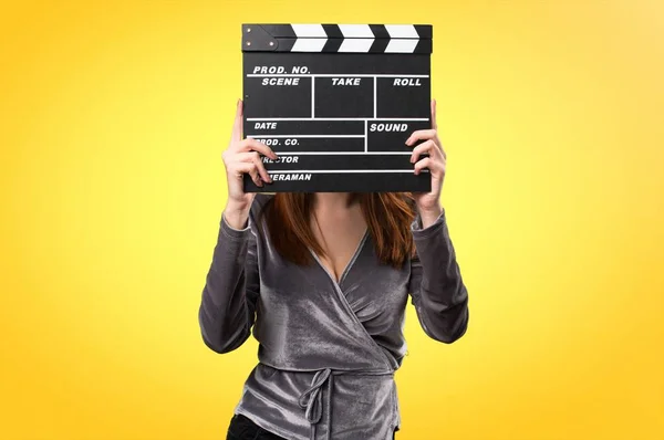 Beautiful young girl holding a clapperboard on colorful background — Stock Photo, Image