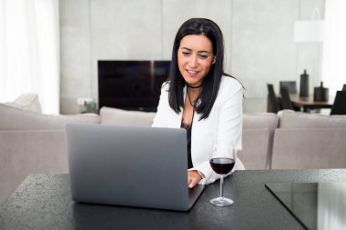 Dizüstü bilgisayarı ve şarap kadehi olan güzel bir genç kız.