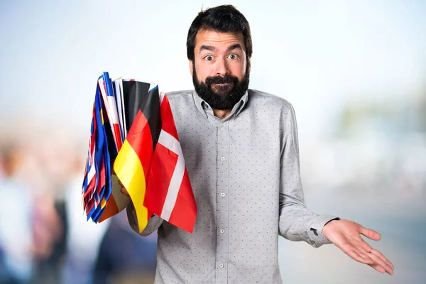 Hombre guapo con barba sosteniendo muchas banderas y haciendo unimportan — Foto de Stock