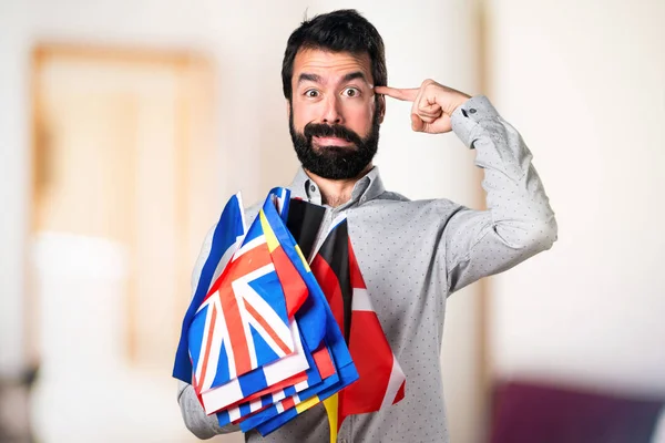 Handsome man with beard holding many flags and making crazy gest — Stock Photo, Image