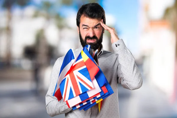 Homem bonito frustrado com barba segurando muitas bandeiras — Fotografia de Stock