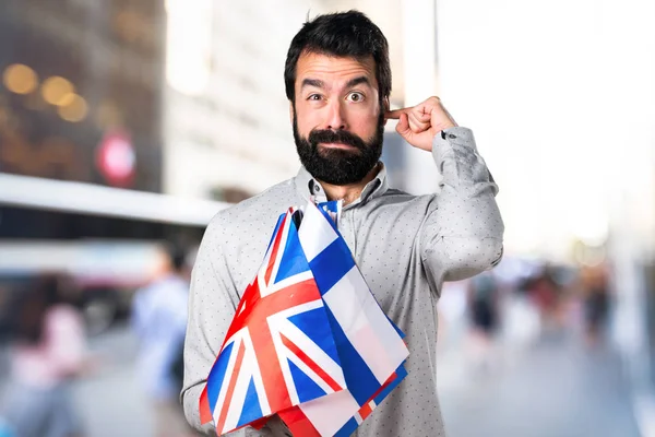 Homem bonito com barba segurando muitas bandeiras e cobrindo seus ouvidos — Fotografia de Stock