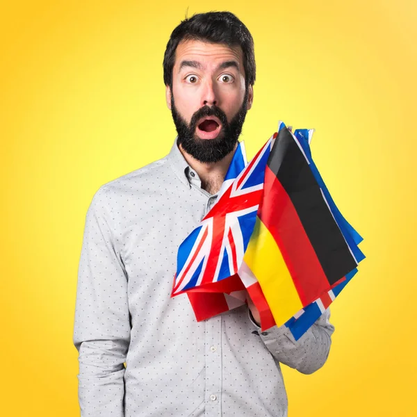 Hombre guapo con barba sosteniendo muchas banderas y haciendo g sorpresa —  Fotos de Stock