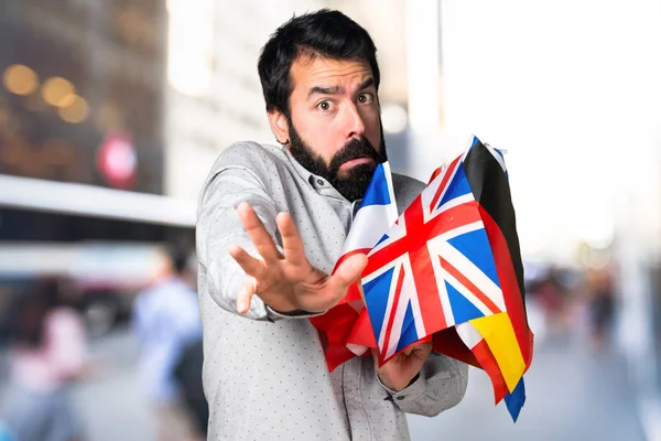 Homem bonito assustado com barba segurando muitas bandeiras — Fotografia de Stock