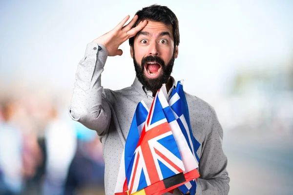 Knappe man met baard houden vele vlaggen en tonen iets — Stockfoto