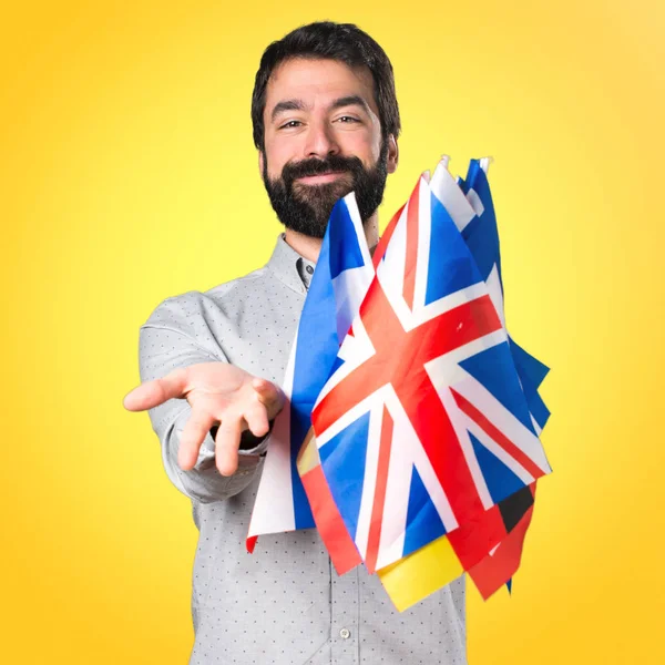 Hombre guapo con barba sosteniendo muchas banderas y presentando algo — Foto de Stock