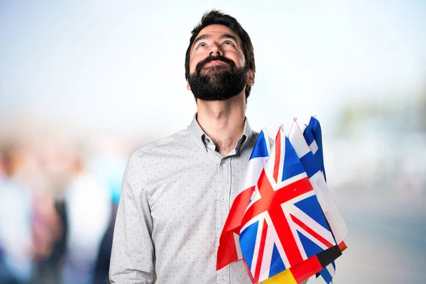 Bell'uomo con la barba che tiene molte bandiere e alza lo sguardo — Foto Stock