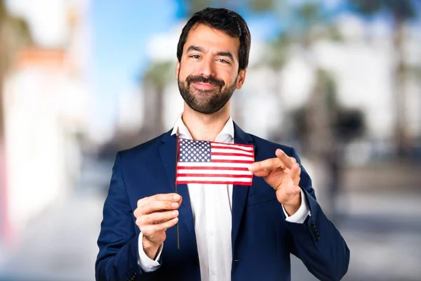 Hombre guapo sosteniendo una bandera americana sobre fondo desenfocado —  Fotos de Stock