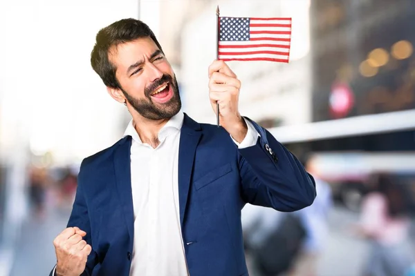 Hombre guapo sosteniendo una bandera americana sobre fondo desenfocado —  Fotos de Stock