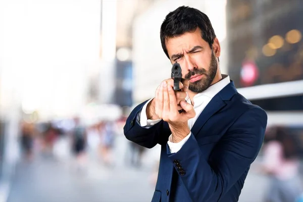 Hombre guapo sosteniendo una pistola sobre un fondo desenfocado — Foto de Stock