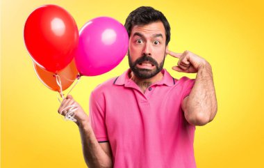Balonlar tutarak ve renkli arka plan üzerinde kulakları kapsayan yakışıklı delikanlı