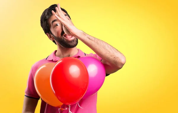 Όμορφος νεαρός άνδρας making έναs αστείο εκμετάλλευση μπαλόνια σε πολύχρωμο φόντο — Φωτογραφία Αρχείου