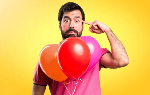 Όμορφος νεαρός άνδρας κάνει τρελό χειρονομία εκμετάλλευση μπαλόνια σε πολύχρωμο φόντο — Φωτογραφία Αρχείου
