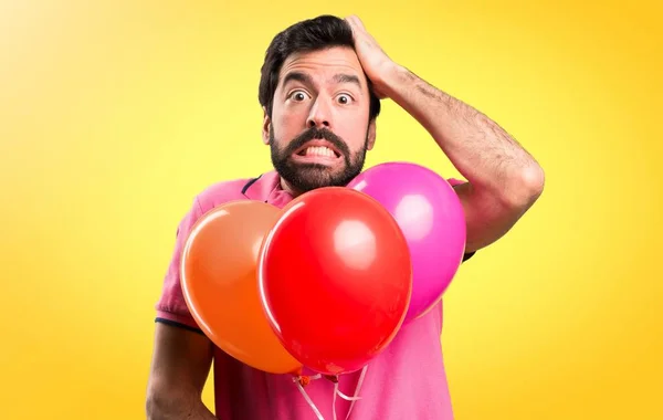 Frusztrált, jóvágású fiatalember gazdaság ballonok színes háttérrel — Stock Fotó