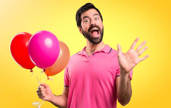 Όμορφος νεαρός άνδρας κρατά μπαλόνια και χαιρετούσαν σε πολύχρωμο φόντο — Φωτογραφία Αρχείου