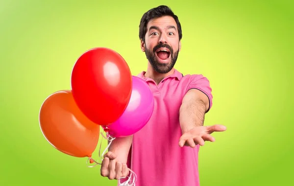 Stilig ung man hålla ballonger och presentera något på färgstarka bakgrund — Stockfoto