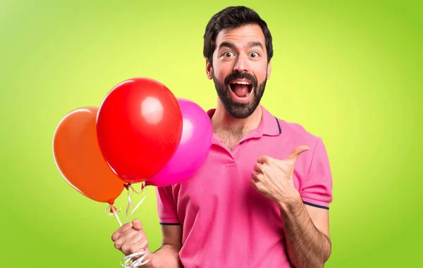 Όμορφος νεαρός άνδρας κρατά μπαλόνια και με τον αντίχειρα επάνω σε πολύχρωμο φόντο — Φωτογραφία Αρχείου
