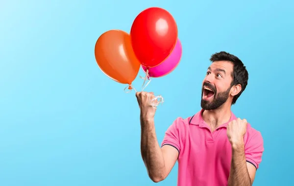 Afortunado joven guapo sosteniendo globos sobre fondo colorido — Foto de Stock