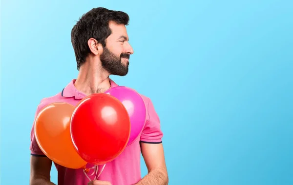 Handsome young man holding balloons and  looking lateral on colorful background