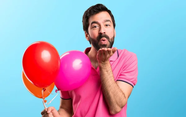 Красивый молодой человек держит воздушные шары и посылает поцелуй на красочном фоне — стоковое фото