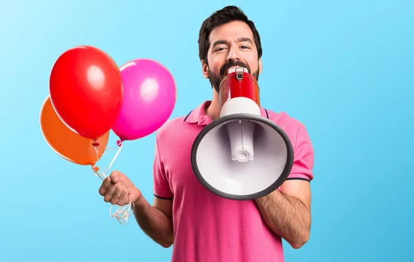 Schöner junger Mann mit Luftballons und Megafon auf buntem Hintergrund — Stockfoto