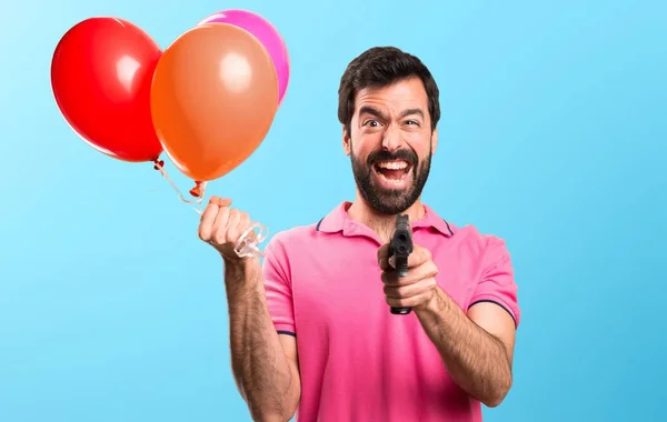 Όμορφος νεαρός άνδρας κρατά μπαλόνια και κρατώντας ένα πιστόλι σε πολύχρωμο φόντο — Φωτογραφία Αρχείου