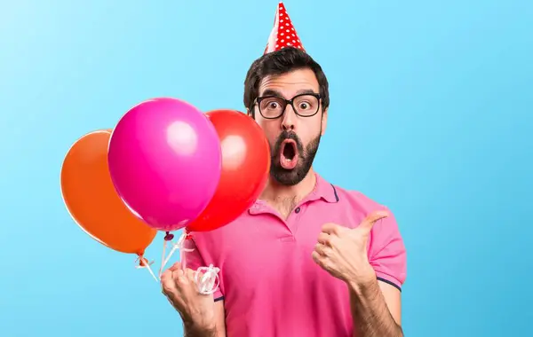 Lucky handsome young man holding balloons on colorful background