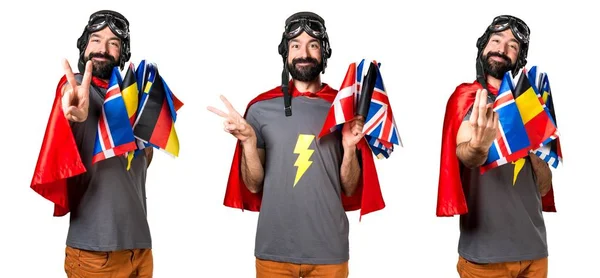 Superhéroe con un montón de banderas haciendo gesto de victoria — Foto de Stock