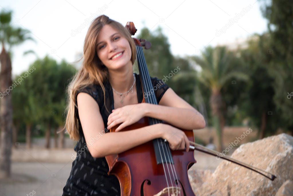 Happy young beautiful girl with her cello on the outside