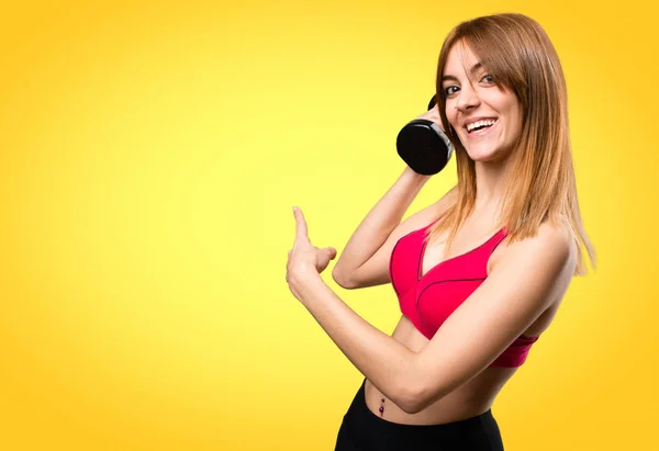 Mulher esporte bonita com halteres apontando para trás em b colorido — Fotografia de Stock