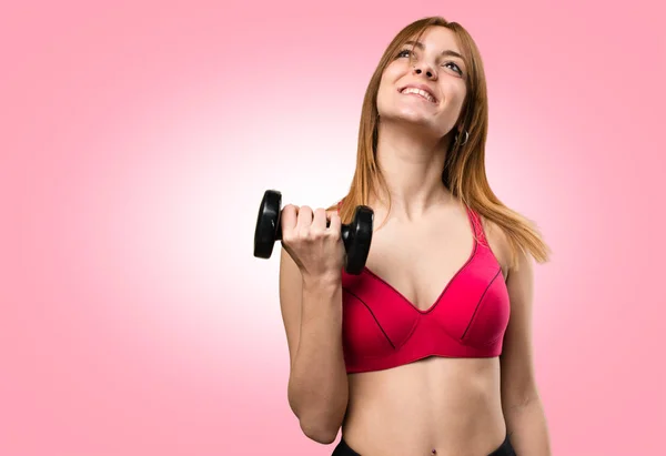 Beautiful sport woman with dumbbells looking up on colorful back — Stock Photo, Image