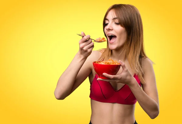 Giovane donna sportiva mangiare cereali da una ciotola su backgro colorato — Foto Stock