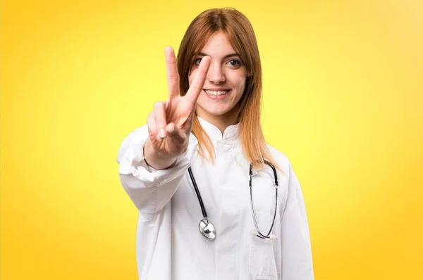 Jovem médico mulher contando dois em fundo colorido — Fotografia de Stock