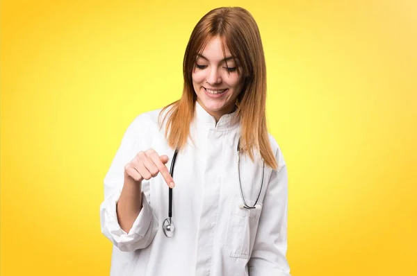 Jonge dokter woman wijzend naar beneden op de kleurrijke achtergrond — Stockfoto