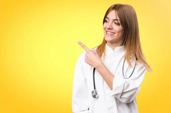 Jonge dokter vrouw wijzend naar de laterale op kleurrijke achtergrond — Stockfoto