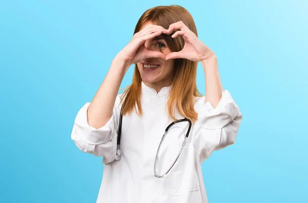 Jovem médico mulher fazendo um coração com as mãos no fundo colorido — Fotografia de Stock