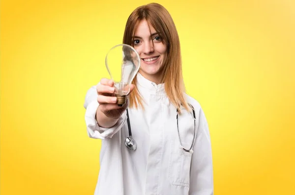 Fiatal orvos nő gazdaság egy izzó, színes háttérrel — Stock Fotó