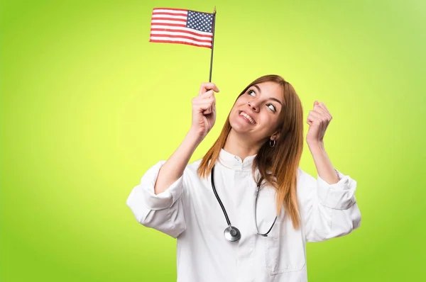 Joven doctora sosteniendo una bandera americana sobre fondo colorido —  Fotos de Stock
