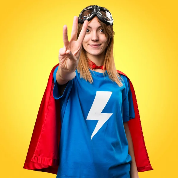 Pretty superhero girl counting three on colorful background