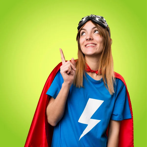 Pretty superhero girl pointing up on colorful background