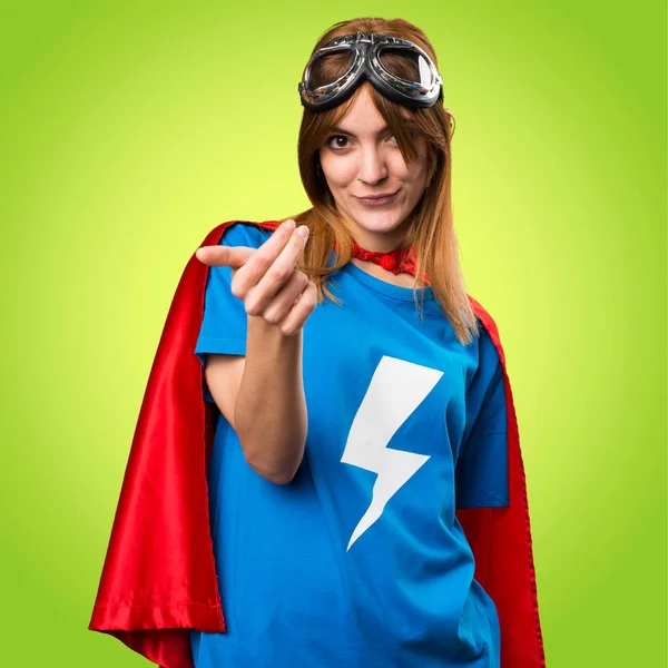 Pretty superhero girl doing coming gesture on colorful backgroun